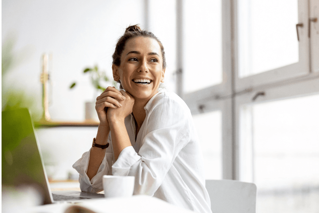 Female sitting at a table with a laptop and smiling